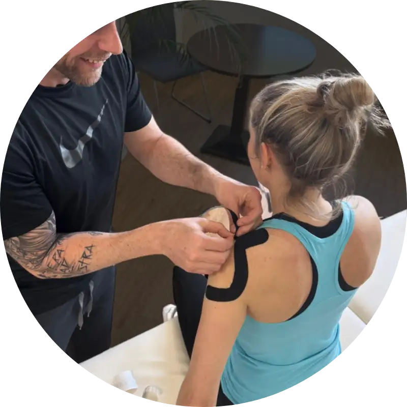 Sporttherapeut bringt schwarzes Kinesiotape auf der Schulter einer Patientin an.