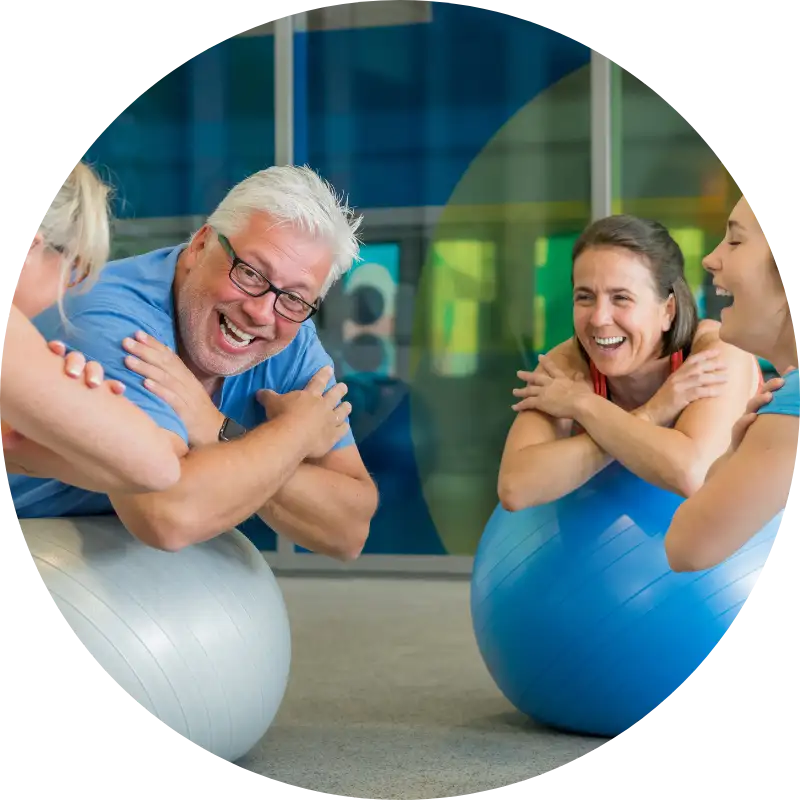 Erwachsene trainieren gemeinsam lachend auf Gymnastikbällen bei Gruppenkurs.